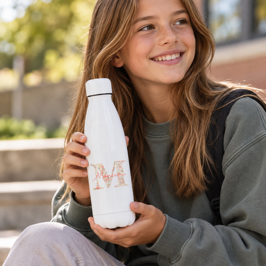 Botella termo blanca Pacífico personalizada con inicial Liberty en tonos coral y nombre, niña sonriendo con ella en las manos
