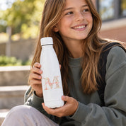 Botella termo blanca Pacífico personalizada con inicial Liberty en tonos coral y nombre, niña sonriendo con ella en las manos