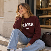 Sudadera burdeos personalizada "Mamá" estilo college con año, mujer sentada en un escalón de la calle